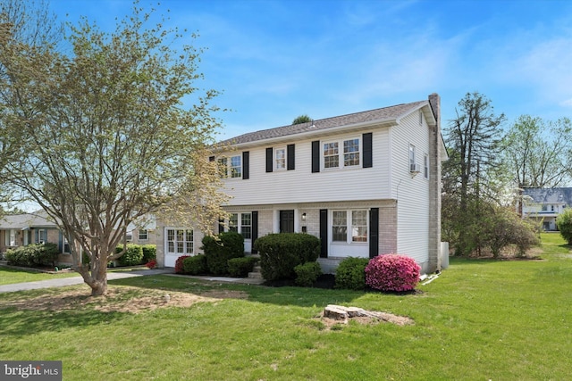 colonial home featuring a chimney, a front lawn, and brick siding