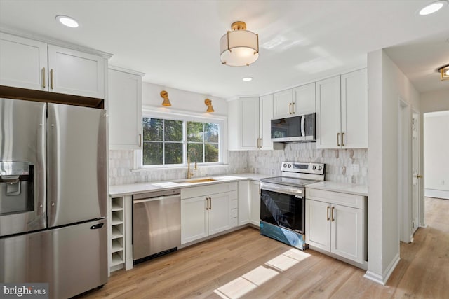 kitchen with backsplash, a sink, light countertops, light wood finished floors, and stainless steel appliances
