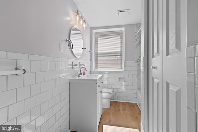 full bathroom featuring toilet, wood finished floors, tile walls, wainscoting, and vanity