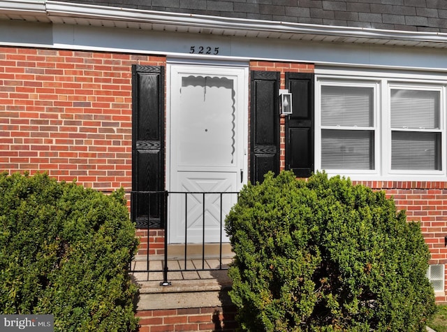 view of exterior entry featuring brick siding and roof with shingles