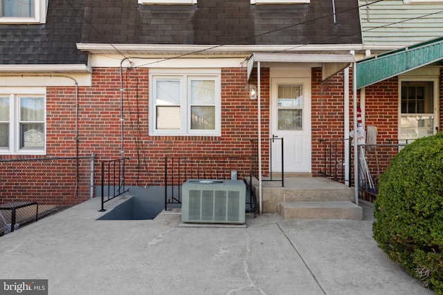 entrance to property with cooling unit, a patio area, brick siding, and a shingled roof