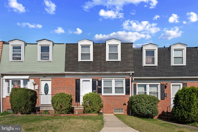 view of front of house featuring roof with shingles, a front lawn, brick siding, and mansard roof