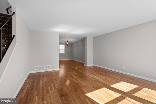 unfurnished living room featuring visible vents, wood finished floors, baseboards, and stairs