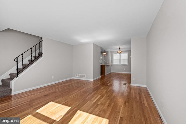 unfurnished living room featuring visible vents, wood finished floors, baseboards, and stairs