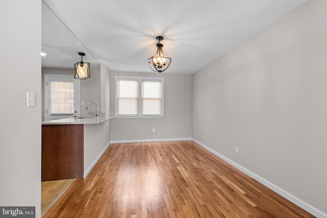 unfurnished dining area featuring baseboards, light wood-style floors, a chandelier, and a sink