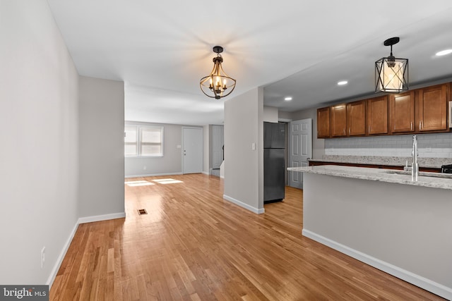 kitchen with freestanding refrigerator, decorative light fixtures, baseboards, a sink, and tasteful backsplash