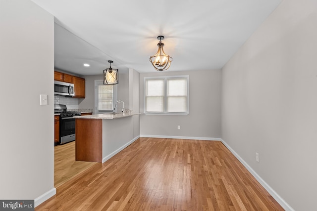 kitchen with a notable chandelier, range with gas cooktop, light wood-type flooring, stainless steel microwave, and baseboards