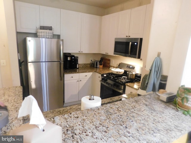 kitchen with stainless steel appliances, light stone countertops, and white cabinetry