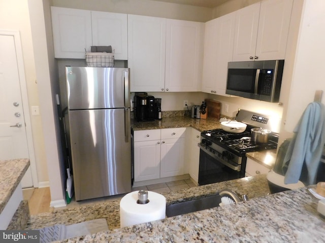 kitchen featuring white cabinets, stainless steel appliances, light stone counters, and a sink