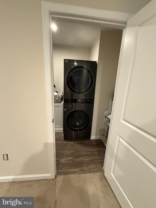 clothes washing area with baseboards, stacked washer and clothes dryer, wood finished floors, and laundry area