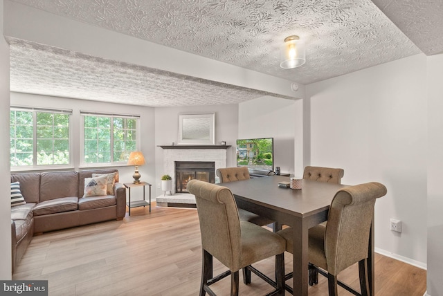 8337 Wind Fall Rd, Springfield, VA 22153 - dining area with a textured ceiling, light wood-style floors, a brick fireplace, and baseboards