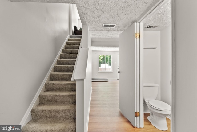 8337 Wind Fall Rd, Springfield, VA 22153 - stairway featuring wood finished floors, a textured ceiling, baseboard heating, and baseboards