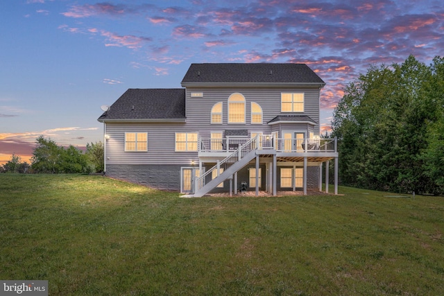back of house at dusk featuring stairway, a deck, a lawn, and roof with shingles