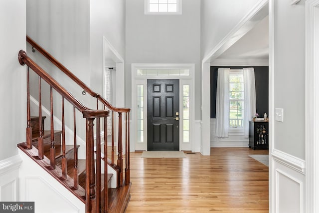 foyer entrance with a decorative wall, light wood finished floors, a towering ceiling, a wainscoted wall, and stairway