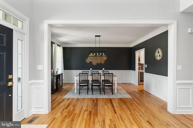 dining area with a chandelier, crown molding, plenty of natural light, light wood-style flooring, and wainscoting