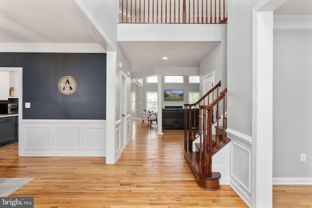 foyer entrance with stairs, light wood finished floors, ornamental molding, wainscoting, and a decorative wall