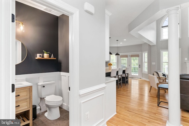 bathroom featuring a wainscoted wall, plenty of natural light, wood finished floors, toilet, and a decorative wall