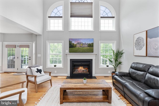 living room with a towering ceiling, healthy amount of natural light, wood finished floors, a fireplace with flush hearth, and baseboards