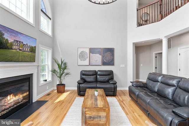 living room featuring a towering ceiling, wood finished floors, a glass covered fireplace, and baseboards
