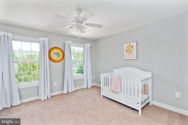 bedroom featuring a crib, carpet flooring, baseboards, and a ceiling fan