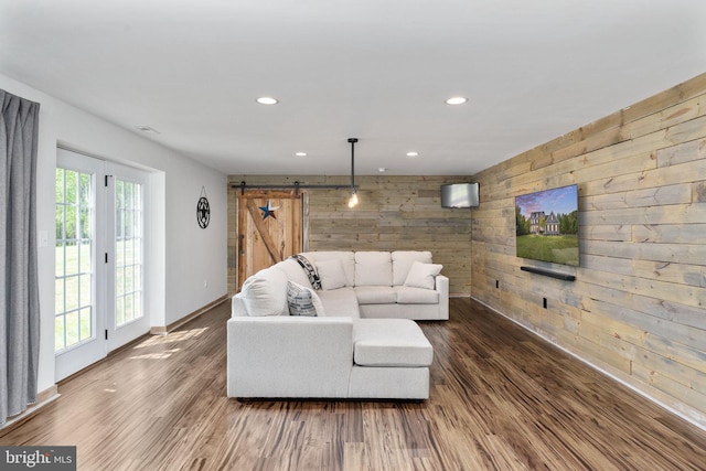 living room featuring wood walls, baseboards, recessed lighting, a barn door, and wood finished floors