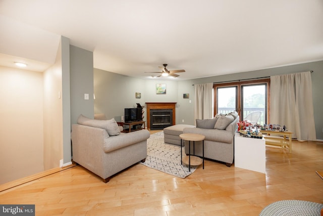 living room featuring light wood finished floors, a ceiling fan, and a glass covered fireplace