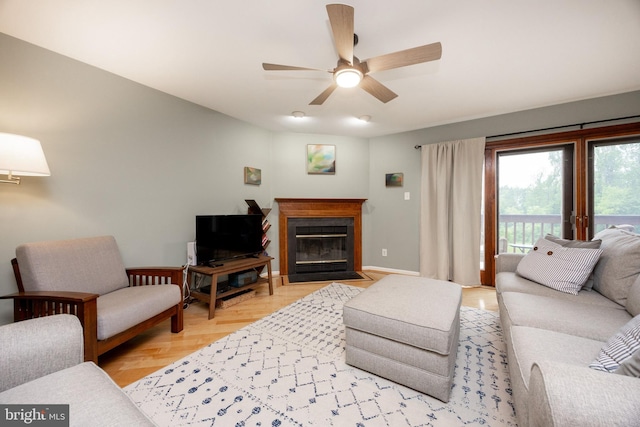 living room featuring a fireplace with flush hearth, baseboards, and a ceiling fan