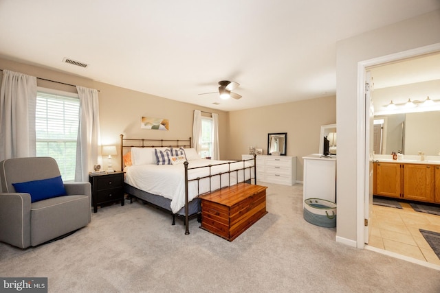 bedroom with light colored carpet, ensuite bathroom, visible vents, and a ceiling fan