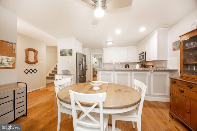 dining space featuring light wood finished floors, a ceiling fan, and stairs
