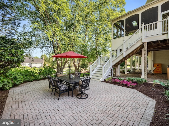 view of patio / terrace featuring stairway, a sunroom, and outdoor dining area