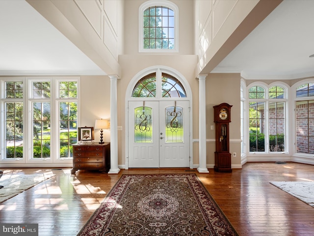 foyer entrance featuring decorative columns, hardwood / wood-style flooring, a towering ceiling, and crown molding