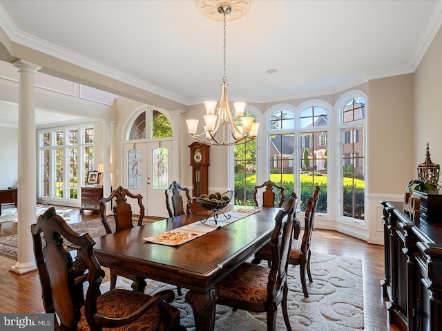 dining room with crown molding, a chandelier, decorative columns, wood finished floors, and a wainscoted wall