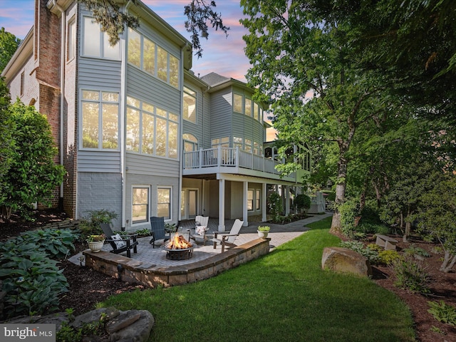 rear view of property featuring an outdoor fire pit, a lawn, a patio area, brick siding, and a wooden deck