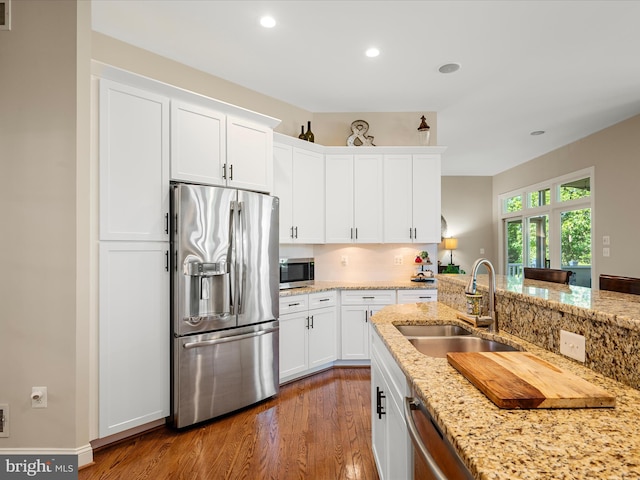 kitchen featuring stainless steel appliances, a sink, wood finished floors, white cabinets, and recessed lighting