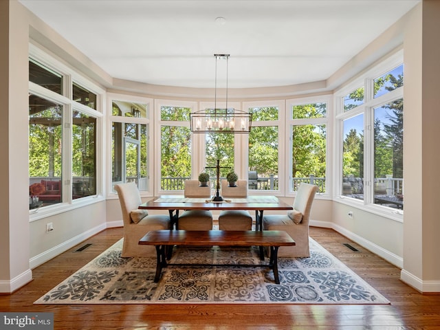 sunroom / solarium featuring baseboards, hardwood / wood-style floors, and a chandelier