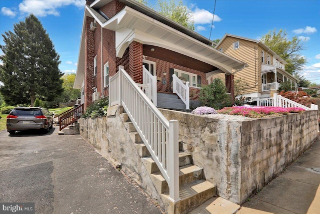 exterior space with covered porch, brick siding, driveway, and stairs