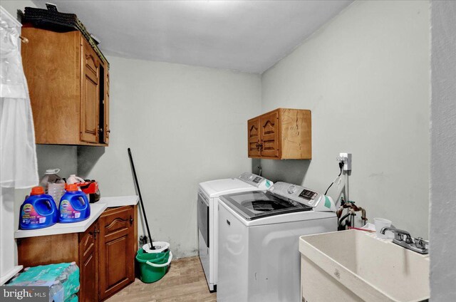 laundry room with cabinet space, washer and clothes dryer, light wood finished floors, and a sink