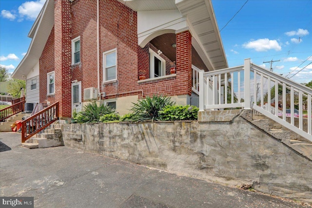 view of side of property with brick siding, central AC unit, and stairs
