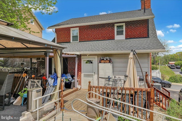 back of house with a chimney, a wooden deck, brick siding, and a shingled roof