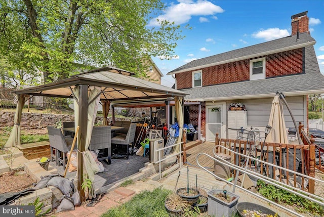 back of property featuring a gazebo, brick siding, outdoor dining space, a chimney, and a shingled roof