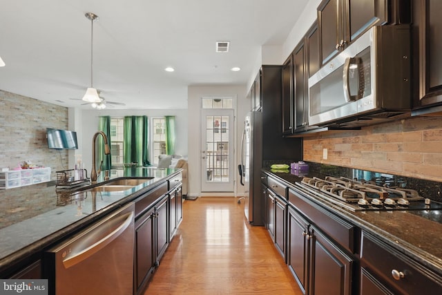 kitchen featuring appliances with stainless steel finishes, decorative backsplash, a sink, and dark stone countertops