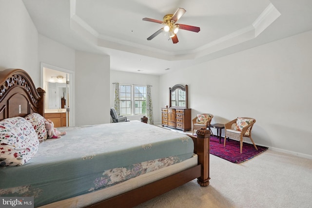 carpeted bedroom with a tray ceiling, ceiling fan, ornamental molding, and ensuite bathroom