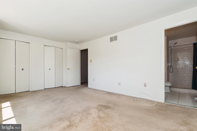 unfurnished bedroom featuring two closets, visible vents, carpet floors, and connected bathroom