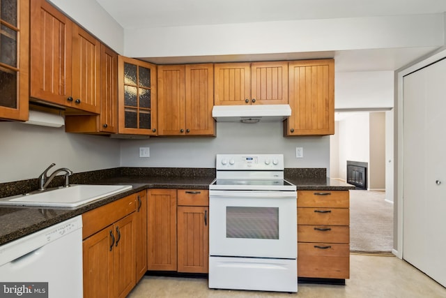 kitchen featuring brown cabinets, a sink, glass insert cabinets, under cabinet range hood, and white appliances