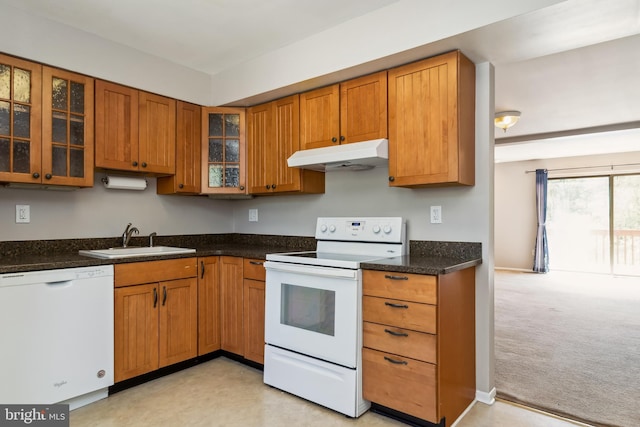 kitchen with brown cabinetry, a sink, glass insert cabinets, under cabinet range hood, and white appliances