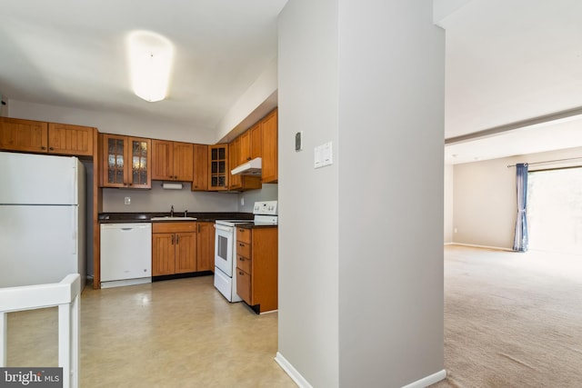 kitchen with brown cabinetry, dark countertops, white appliances, under cabinet range hood, and a sink