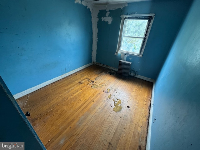 spare room with radiator heating unit, baseboards, and wood-type flooring