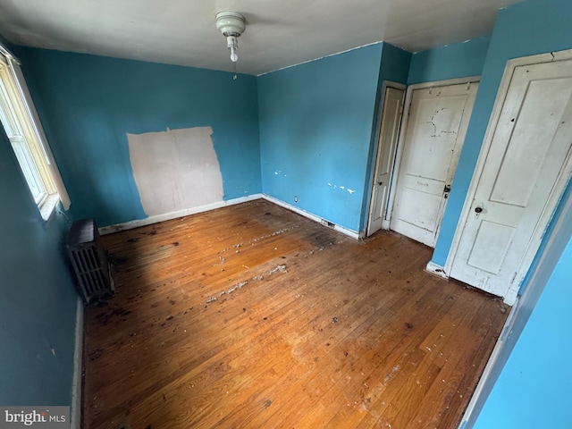 unfurnished bedroom featuring baseboards, a wall mounted AC, and hardwood / wood-style flooring
