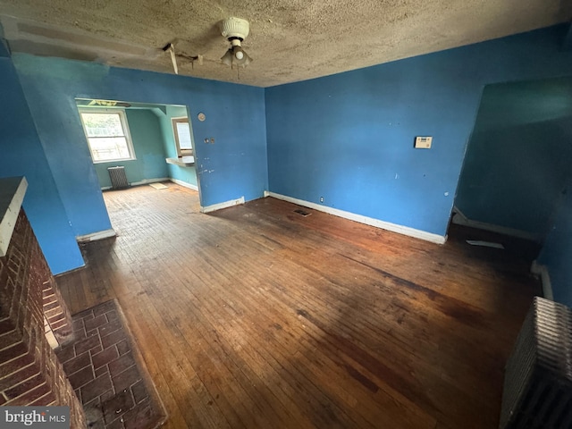 interior space featuring baseboards, a ceiling fan, a textured ceiling, and hardwood / wood-style flooring