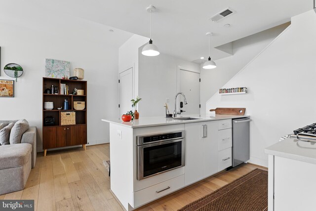 kitchen with a sink, stainless steel appliances, light wood-type flooring, open floor plan, and white cabinetry